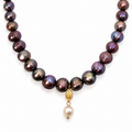 Close-up of the Dark Pearl Necklace’s iridescent pearls, gold medallion and single white pearl drop
